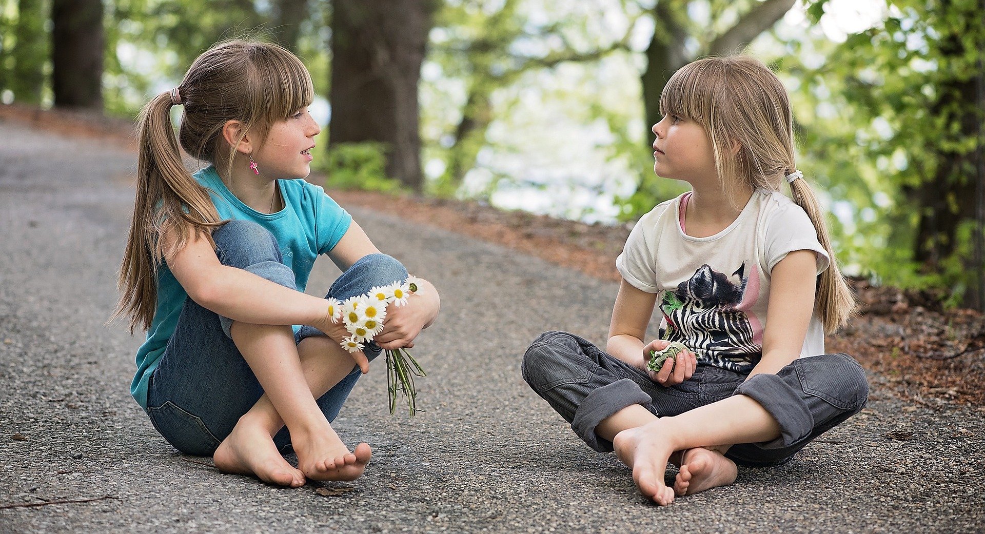 2 girls is seating at the road in the park and having a conversation