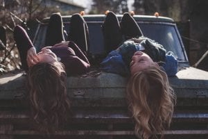 two woman lying down on a car