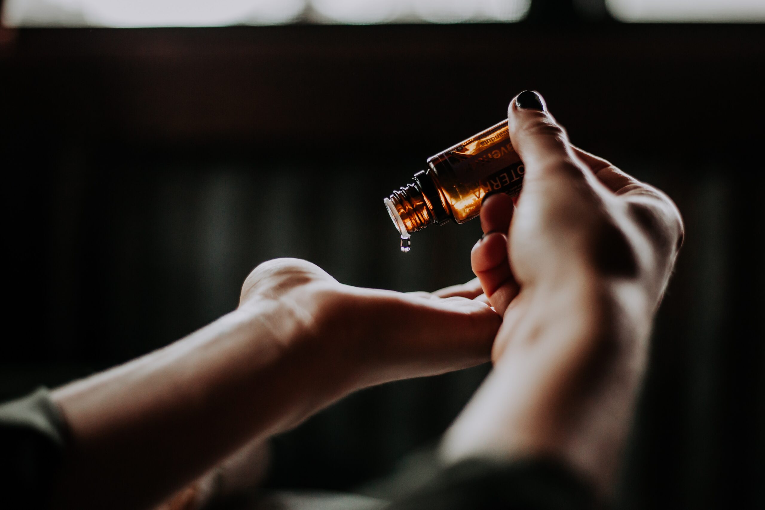 - close-up photo focused on essential oil on amber bottle about to be poured into left hand